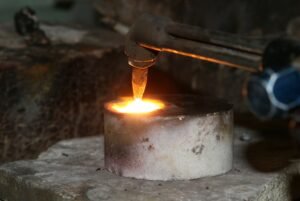 A close-up view of a metal smelting process using a torch, illustrating heat and sparks.