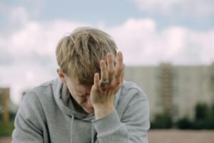 A young man outdoors holding his head in stress, depicting mental health challenges.